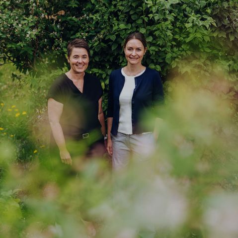 Zwei Frauen vor grüner Hecke